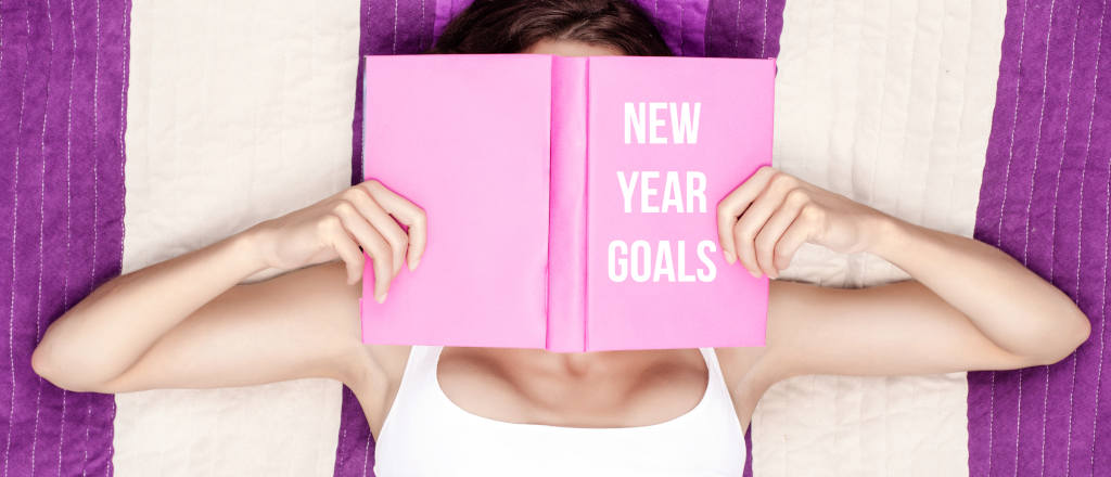 girl lying down with book on her face that says new year golas